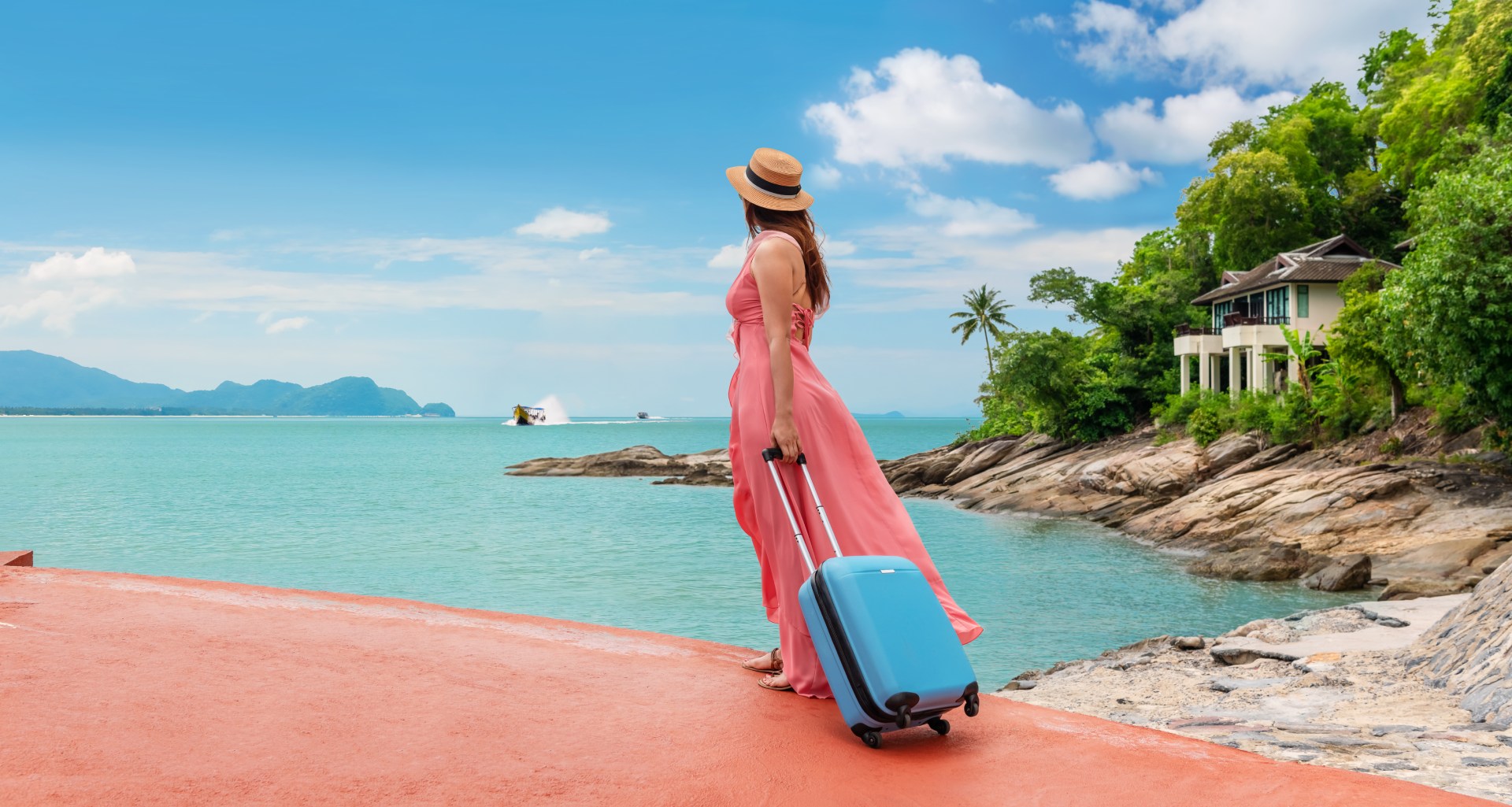 Woman with suitcase in front of the sea and villa to the right